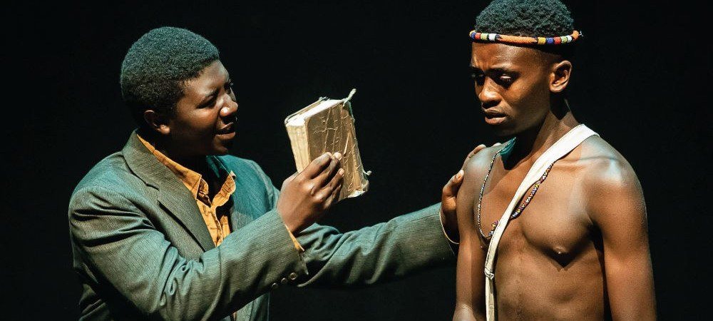 Two actors mid-scene, one holding a book